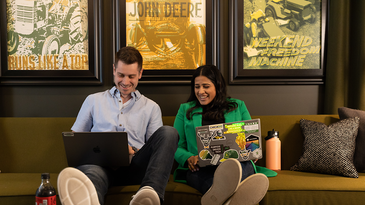 Two colleagues relax on a couch together while working on laptops