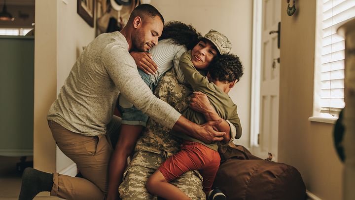 A military family gathers in a big hug together in their home