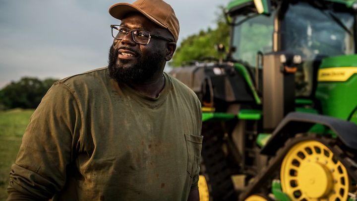 Farmer standing in front of a John Deere tractor.