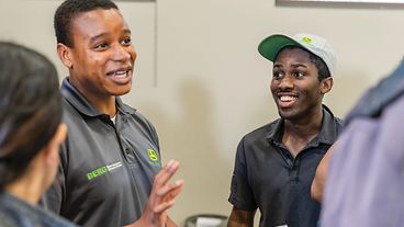John Deere employee holding an open book while talking with students.