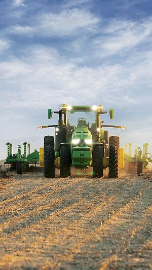 Self-driving John Deere tractor pulling tillage equipment through an open field.