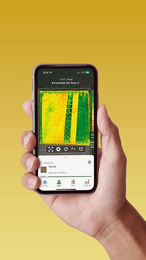Hand holding a smart phone displaying a John Deere Operations Center with fuel rate data.