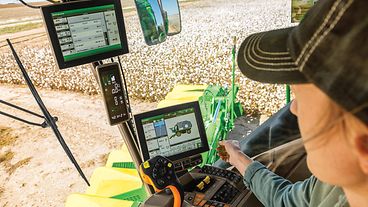 Farmer sitting in a John Deere cotton stripper cab and interacting with the operator display.