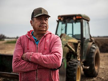 Farmer with arms crossed standing in front of John Deere tractor and looking into the distance.